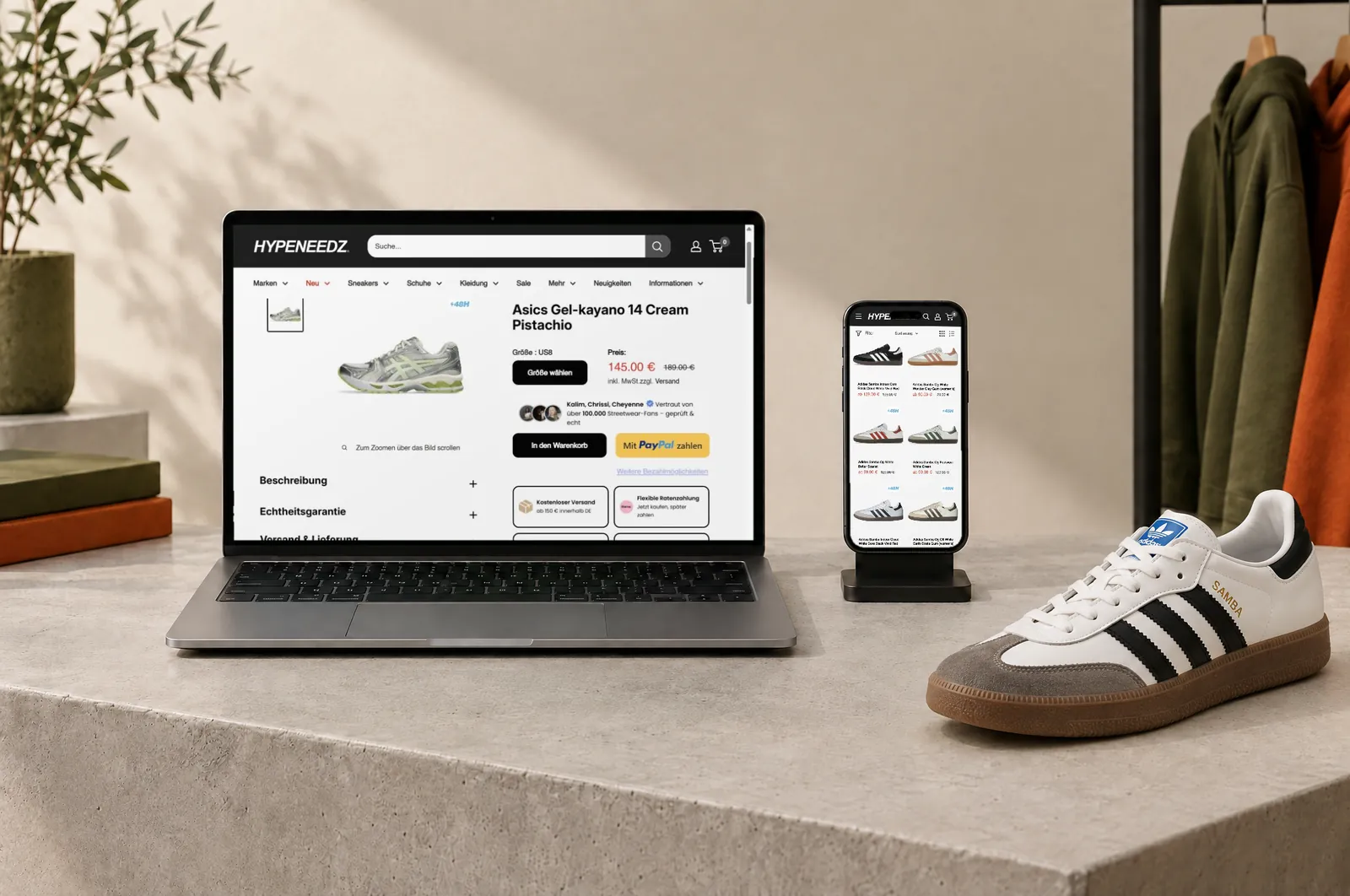 Laptop und Smartphone auf einem Betonsockel, daneben ein Adidas Samba: auf dem Laptop die Produktseite eines Asics-Sneakers im Shopify-Shop hypeneedz.com, auf dem Handy die Kategorie Adidas Samba
